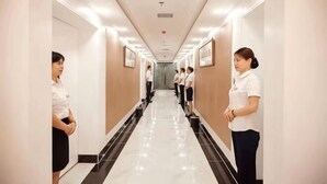Un pasillo de hotel con piso pulido, cuadros en las paredes y un empleado uniformado al final.