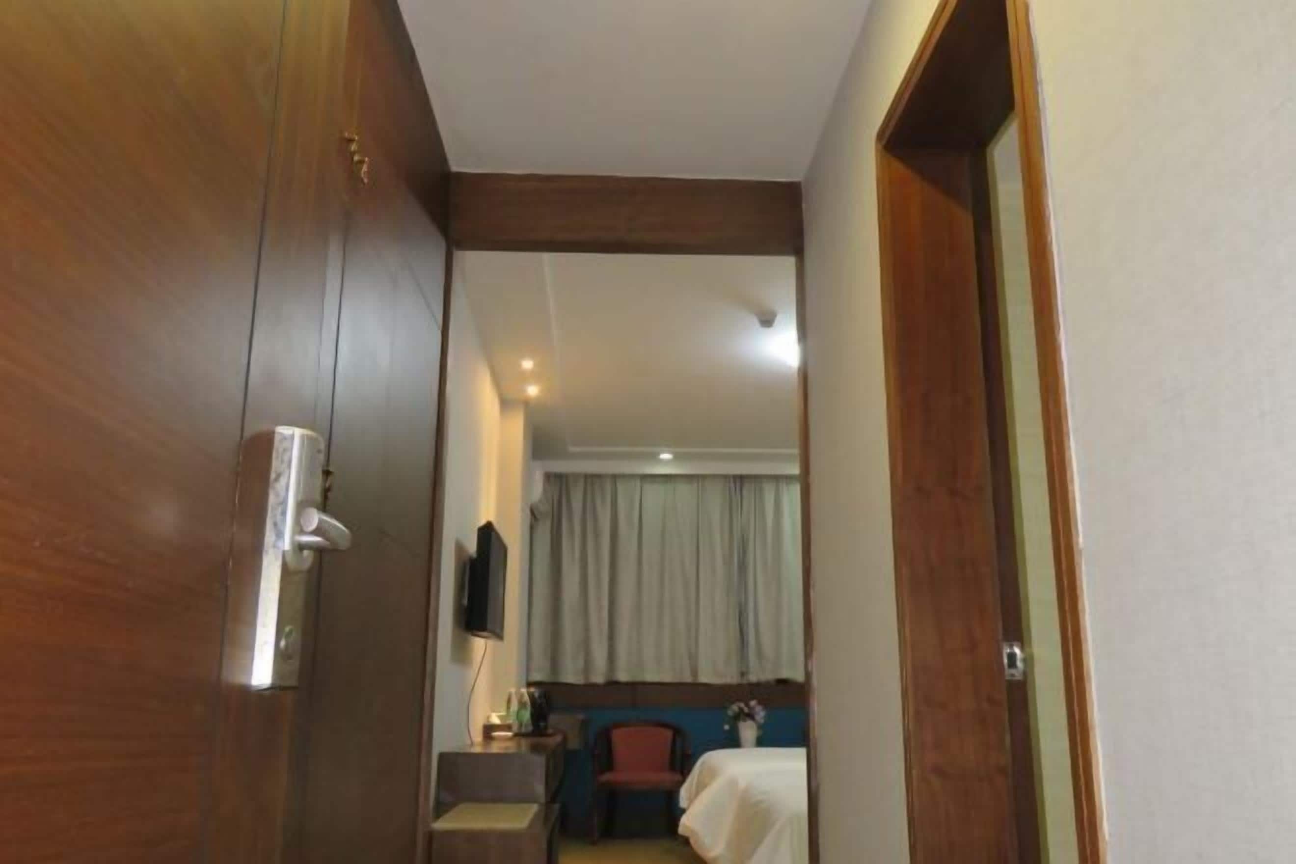 Una camera d'albergo con una porta in legno, un letto con copripiumino bianco, una piccola scrivania con una sedia e un televisore a parete.