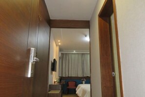 A hotel room with a wooden door, a bed with a white bedspread, a small desk with a chair, and a television on the wall. - Hailian Xianggan Hotel (Yongxin)