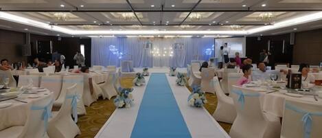 A banquet hall with round tables, a central aisle, and a stage at the front.