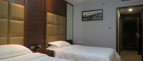 A hotel room with two beds, a large padded headboard, a bedside table, and a framed picture on the wall.