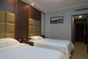 Habitación de hotel con dos camas, un cabecero grande y acolchado, una mesita de noche y un cuadro en la pared.