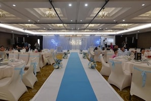 Une salle de banquet avec des tables disposées en rangées, une allée centrale et une scène à l’avant.