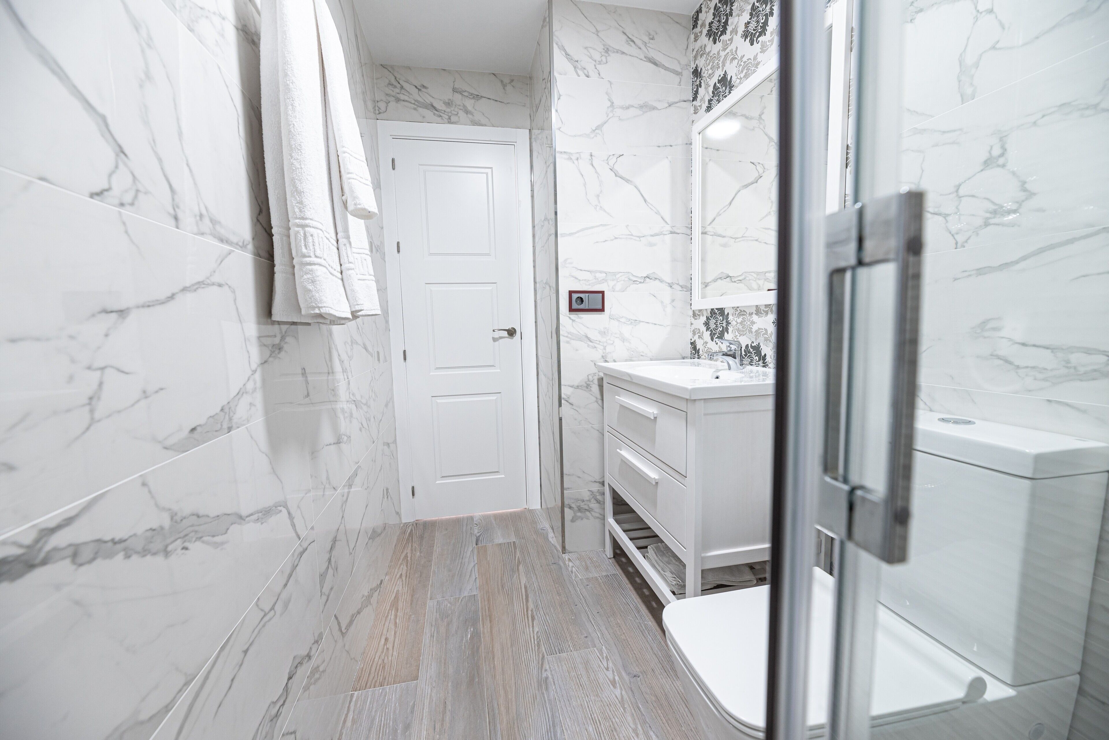 Un baño con paredes de mármol, una puerta blanca, un lavabo y una zona de ducha.