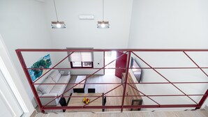 Een modern interieur met een rode metalen scheidingswand, een bank, een eettafel met fruit en hanglampen.