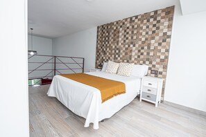 A bedroom with a bed, white nightstands, a wooden headboard, and a patterned wall.