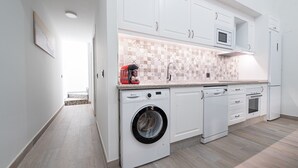 Een moderne keuken met witte kasten, een wasmachine, een magnetron en een vaatwasser.