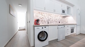Una cocina moderna con muebles blancos, lavadora incorporada, microondas y lavavajillas.