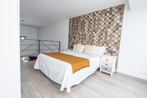 A modern bedroom with a large bed, a wooden headboard, a bedside table with drawers, and a view of the outdoors.