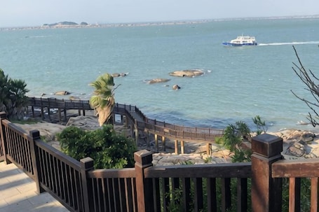 A coastal view with a wooden walkway, rocky shoreline, and a boat on the water.. Chuyang Xiaoshe Hostel