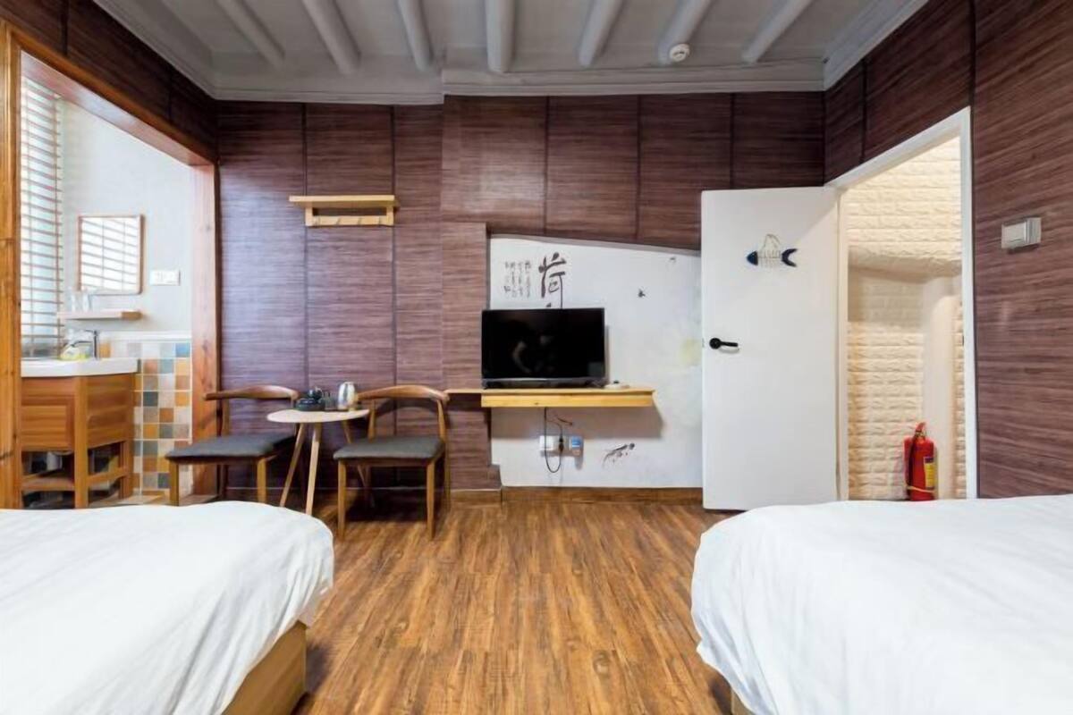 Habitación compacta con dos camas, un escritorio con computadora, una mesita pequeña y sillas.