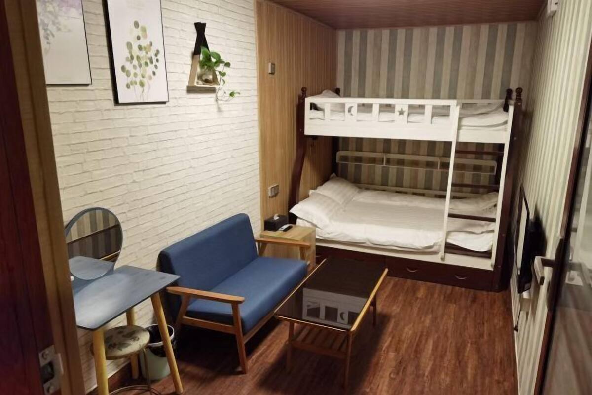 Una habitación compacta con una cama litera, un escritorio pequeño, un sofá azul y una mesa de centro de vidrio.