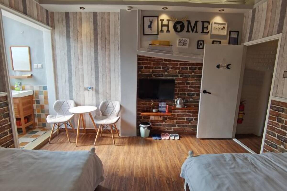 Una habitación con chimenea de ladrillo, televisor, puerta blanca y una pequeña mesa con sillas.