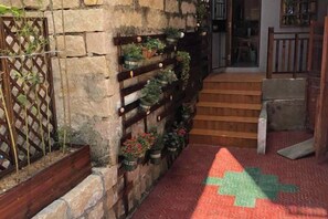 Una pared de piedra con una escalera de madera que conduce a una puerta, una alfombra roja con estampado y un diseño de cruz verde.