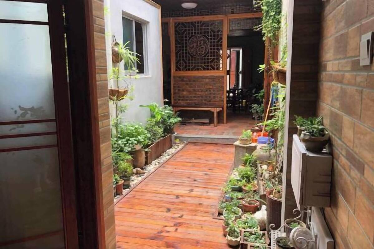 Un estrecho sendero de madera bordeado de plantas en macetas y una pared de ladrillo.