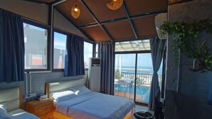 Habitación de hotel con dos camas, suelo de madera, balcón con vistas y techo con diseño de cuadrícula.