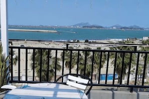 Un balcón con vista al mar, una banca blanca y palmeras.