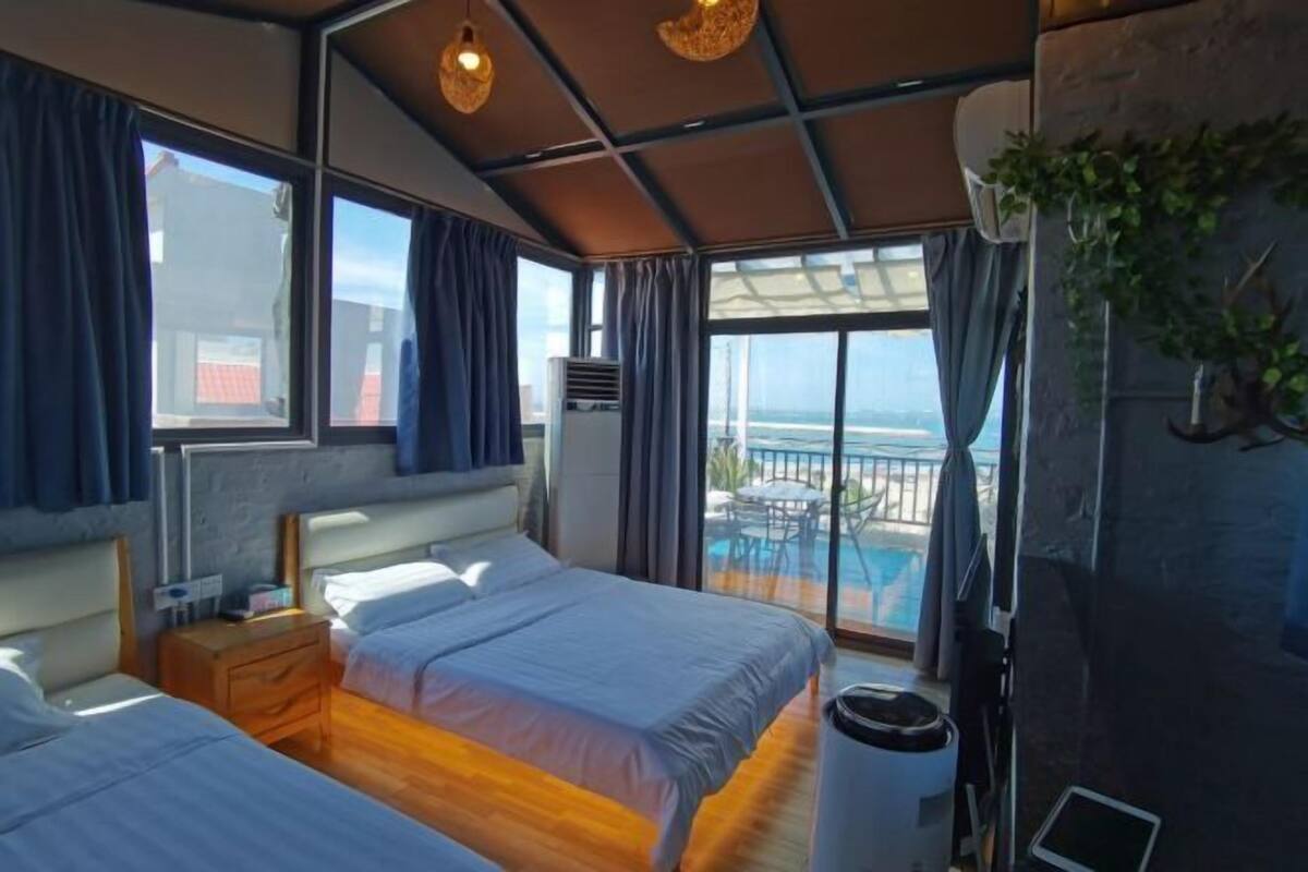 Habitación de hotel con dos camas, un ventanal grande, un balcón y vista al mar.