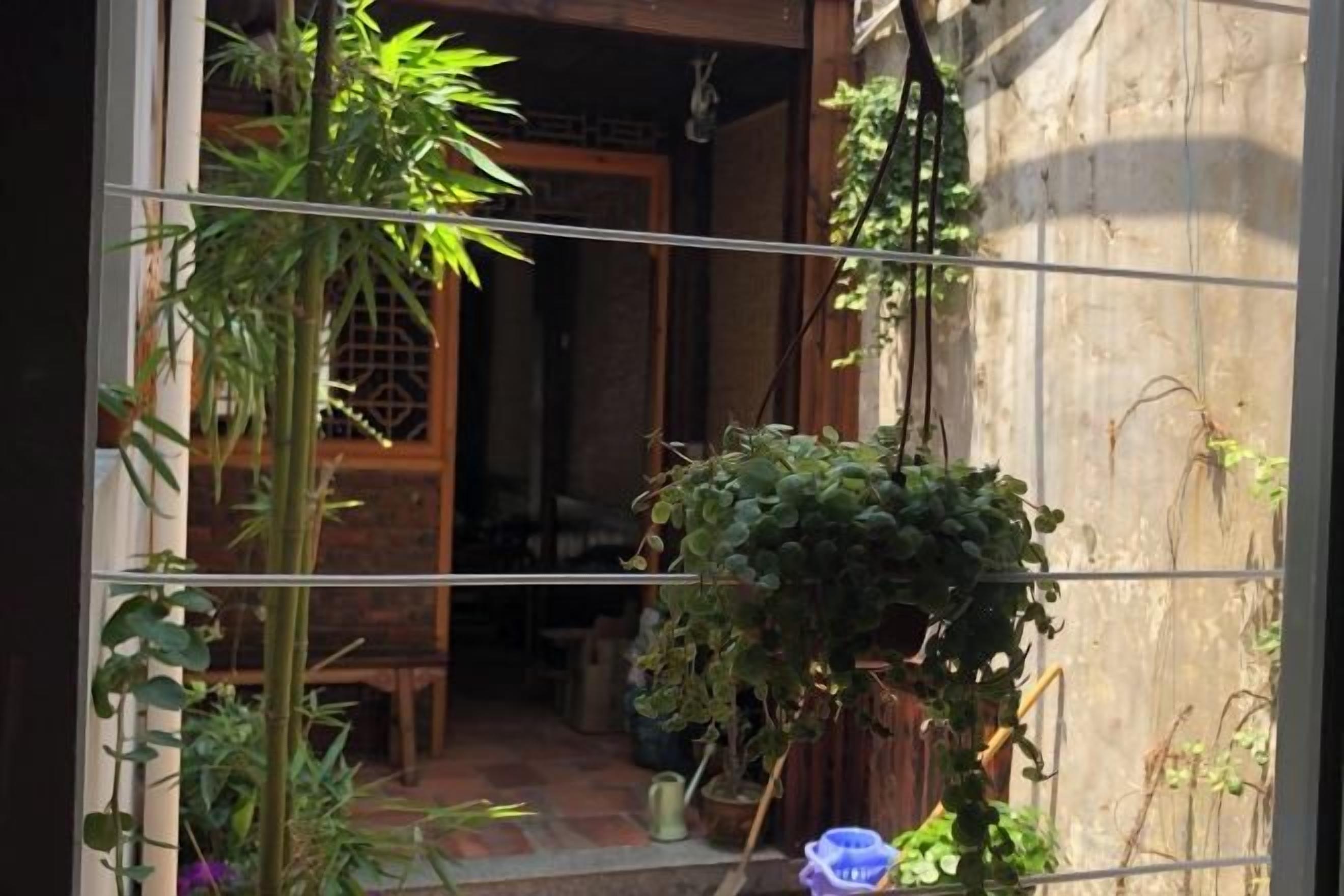 A traditional Japanese entrance with a wooden door, a small garden area with plants, and a tiled floor.