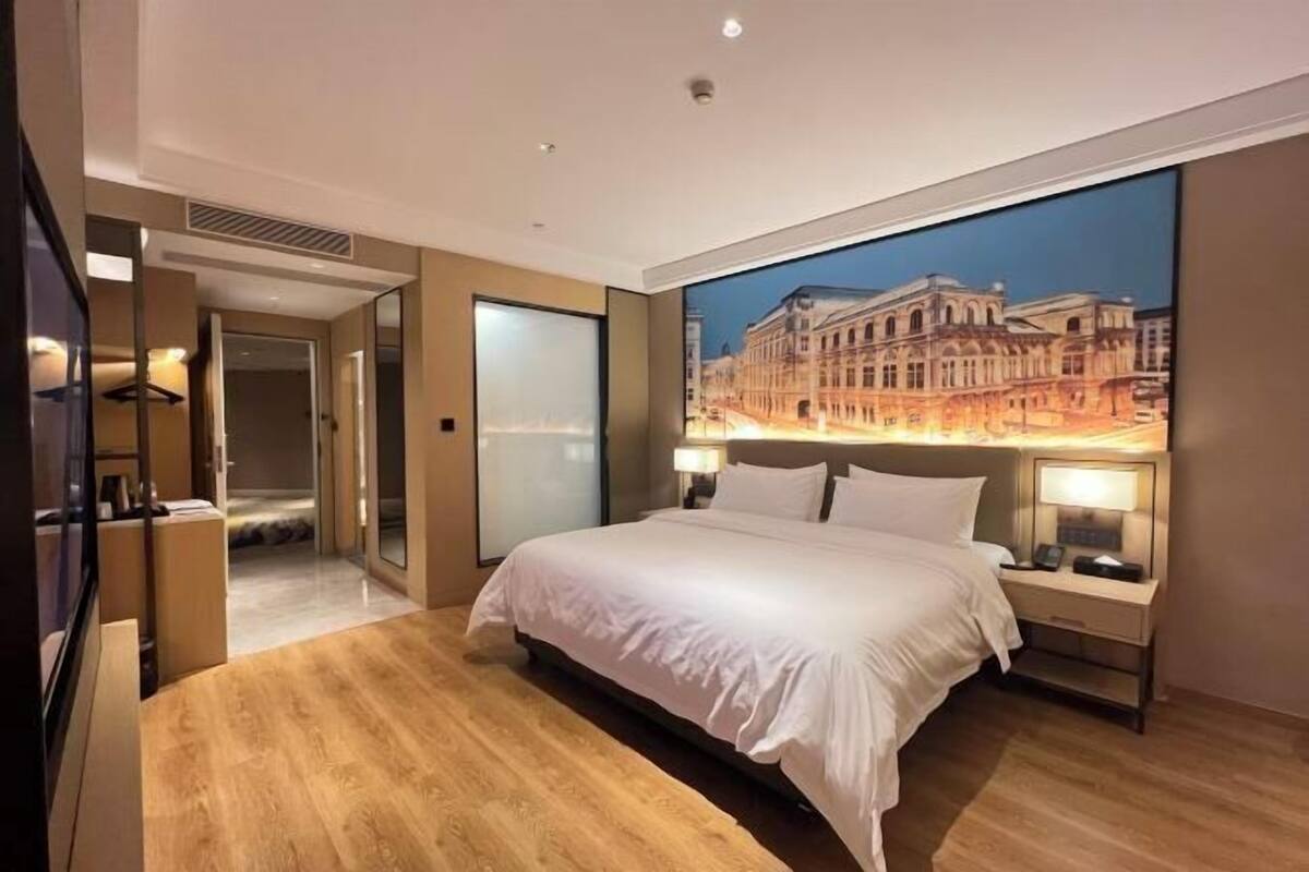 Une chambre d’hôtel moderne dotée d’un grand lit, d’une table de chevet, d’un miroir et offrant une vue sur un bâtiment historique.