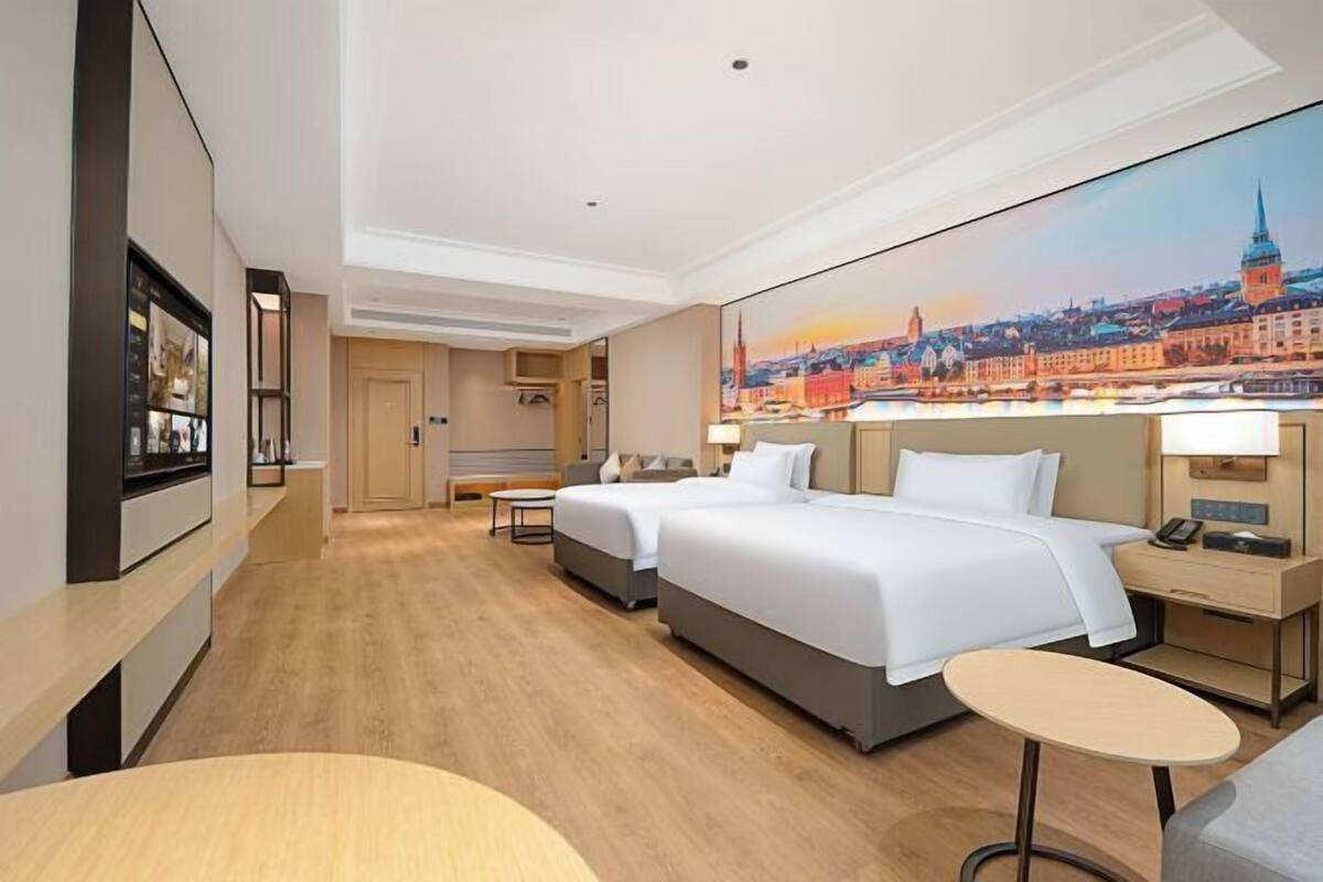 Une chambre d’hôtel avec deux lits, une petite table, une table de chevet et un grand tableau représentant un paysage urbain accroché au mur.