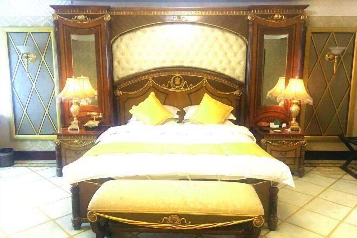 Un grand lit avec une tête de lit, deux tables de chevet avec des lampes et un banc au pied du lit.