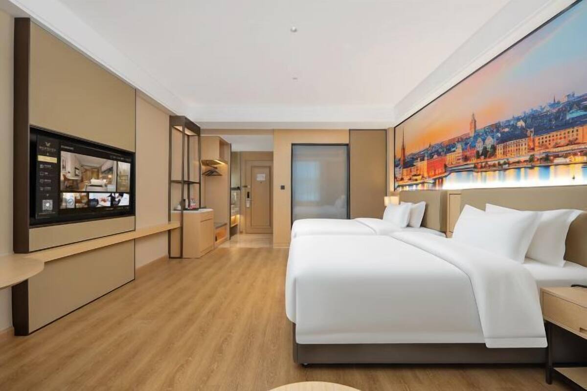 Une chambre d’hôtel moderne avec un grand lit, un téléviseur posé sur un meuble, un tableau représentant un paysage urbain et un plancher en bois.