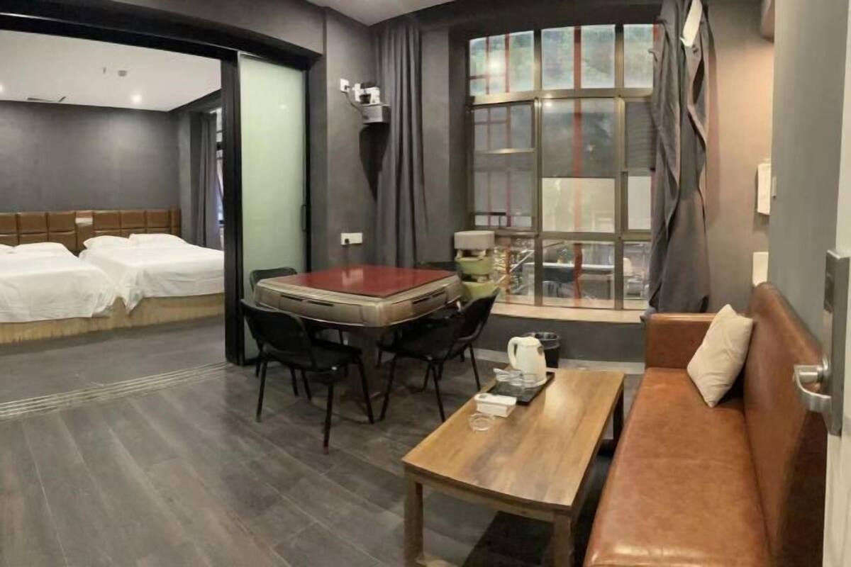 Habitación de hotel con dos camas, una mesa de comedor con sillas, un sofá y un ventanal con cortinas.
