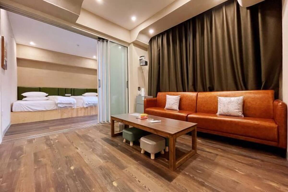 Una habitación de hotel con piso de madera, un sofá, una mesita de centro y una cama con sábanas blancas.