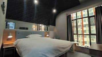A hotel room with a bed, bedside lamps, a small table, a mirror, and a window with curtains.