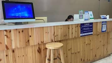 Un mostrador de recepción con un monitor de computadora, una encimera de madera, un taburete y señalización informativa.