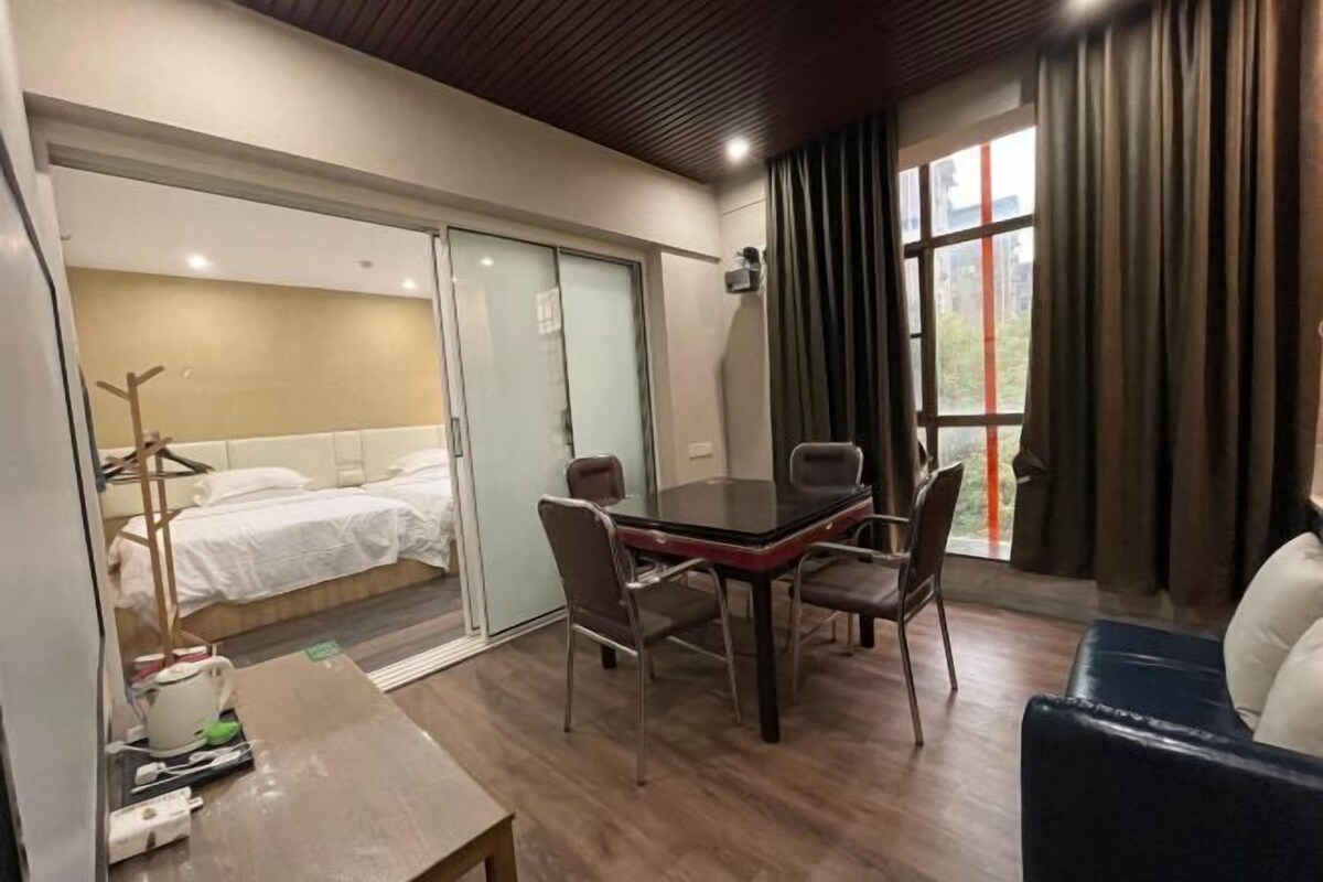 Ein Hotelzimmer mit einem Bett, einem Esstisch mit Stühlen, einer Couch und einem Fenster mit Vorhängen.