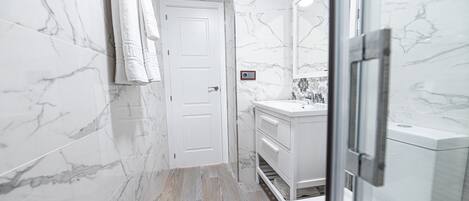 Une salle de bain avec des murs en marbre, une porte blanche, un lavabo et un espace douche.