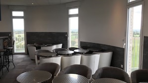 Un interior moderno con mesas y sillas redondas, ventanas amplias y un balcón con vistas.