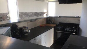 Una cocina con estufa, cafetera y ventana.