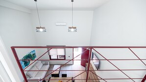 A modern interior with a loft-style living area, a dining table with fruit, and a red metal railing.