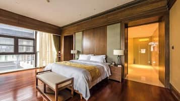 Quarto de hotel com uma cama grande, um banco, uma mesinha de cabeceira, uma janela e uma porta que dá para o banheiro.