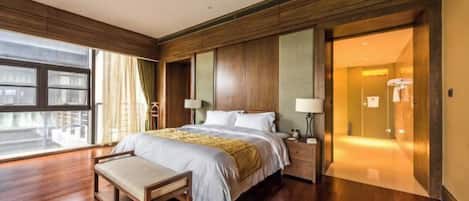 Una habitación de hotel con una cama grande, un banco, una mesita de noche, una ventana y una puerta que da a un baño.