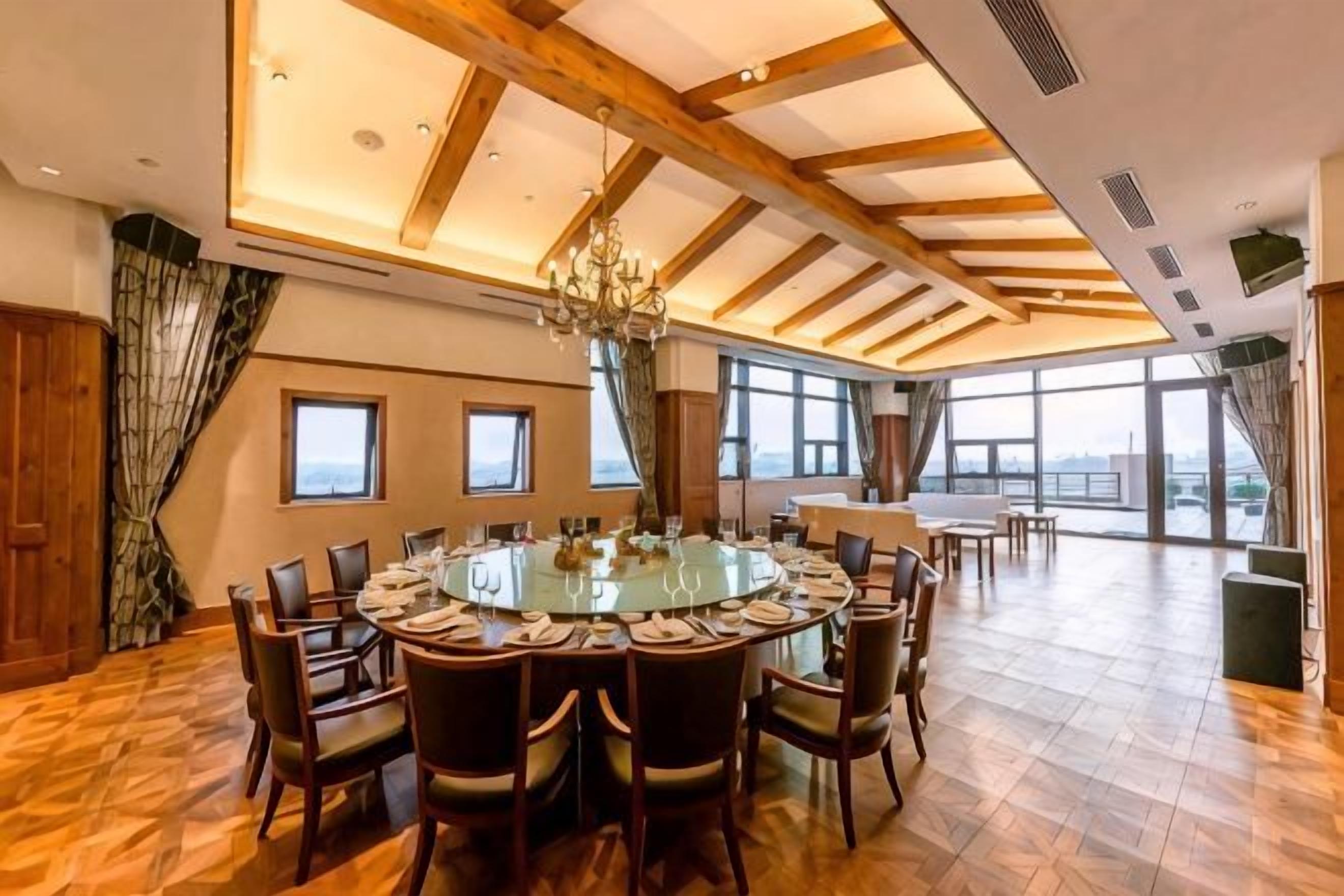 Uma sala de jantar espaçosa com uma mesa redonda cercada por cadeiras, janelas amplas e um teto alto com vigas de madeira.