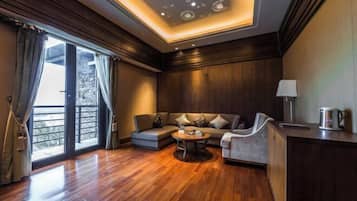 Quarto de hotel moderno com piso de madeira, sofá, mesa de centro redonda, escrivaninha e luminária.