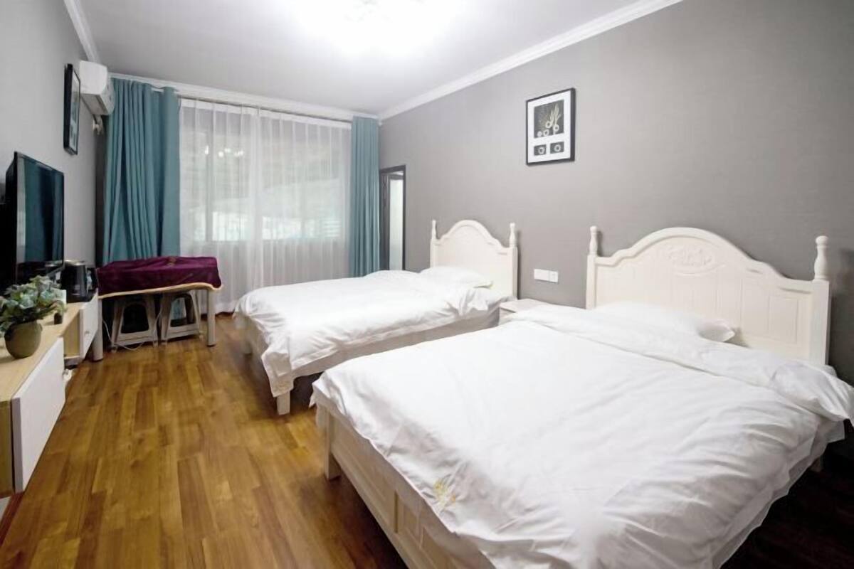 Ein Hotelzimmer mit zwei Einzelbetten, einem Schreibtisch mit Stuhl, einem Fernseher und einem Fenster mit Vorhängen.