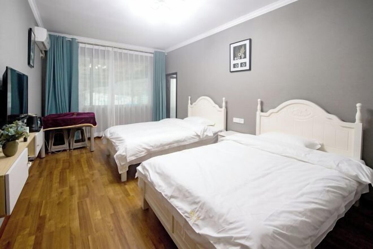 A hotel room with two beds, a desk with a chair, a TV, and a window with curtains.