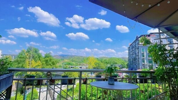Un balcón con mesa y sillas, con vistas a un paisaje urbano y zonas verdes.