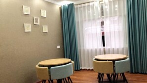 Un comedor con dos mesas redondas y sillas, una ventana con cortinas y cuadros en la pared.