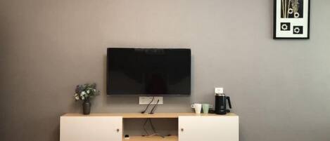 A modern room with a mounted TV, a small coffee station, and a framed picture on the wall.