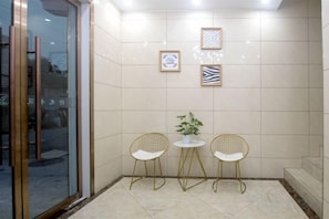 Une petite pièce fermée, avec deux chaises et une table, une plante en pot et des œuvres d’art encadrées accrochées au mur.