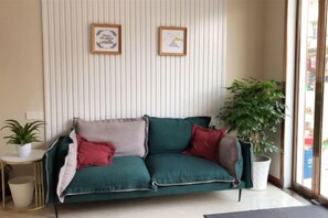 Un canapé vert agrémenté de coussins rouges et gris, une petite table blanche avec une plante, et une plante en pot placée à côté du canapé.