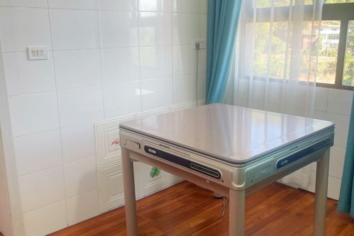 A room with a white tiled wall, a wooden floor, a table with a laptop, and a window with curtains.