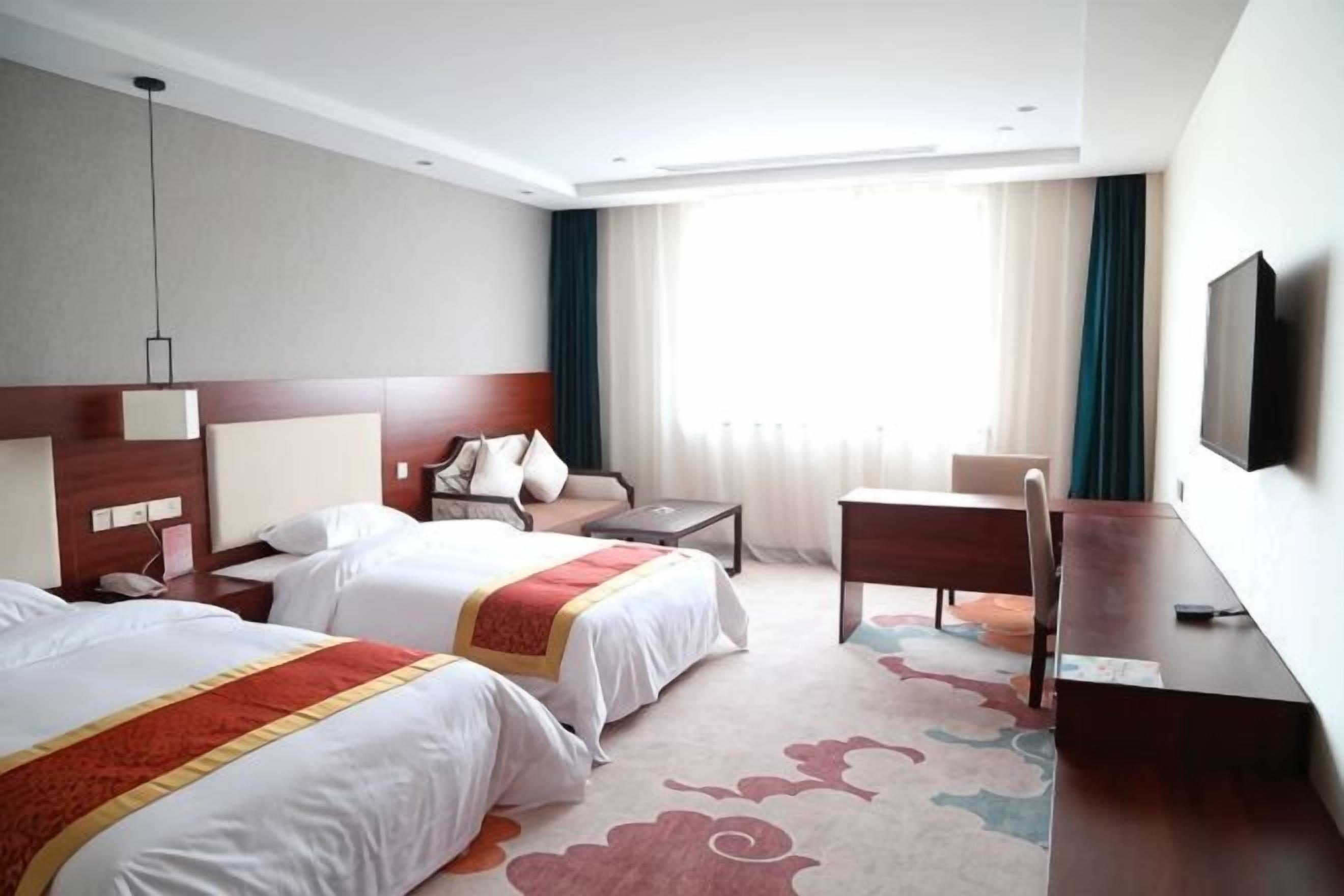 Habitación de hotel con dos camas, un escritorio, una silla, un televisor y una ventana con cortinas.