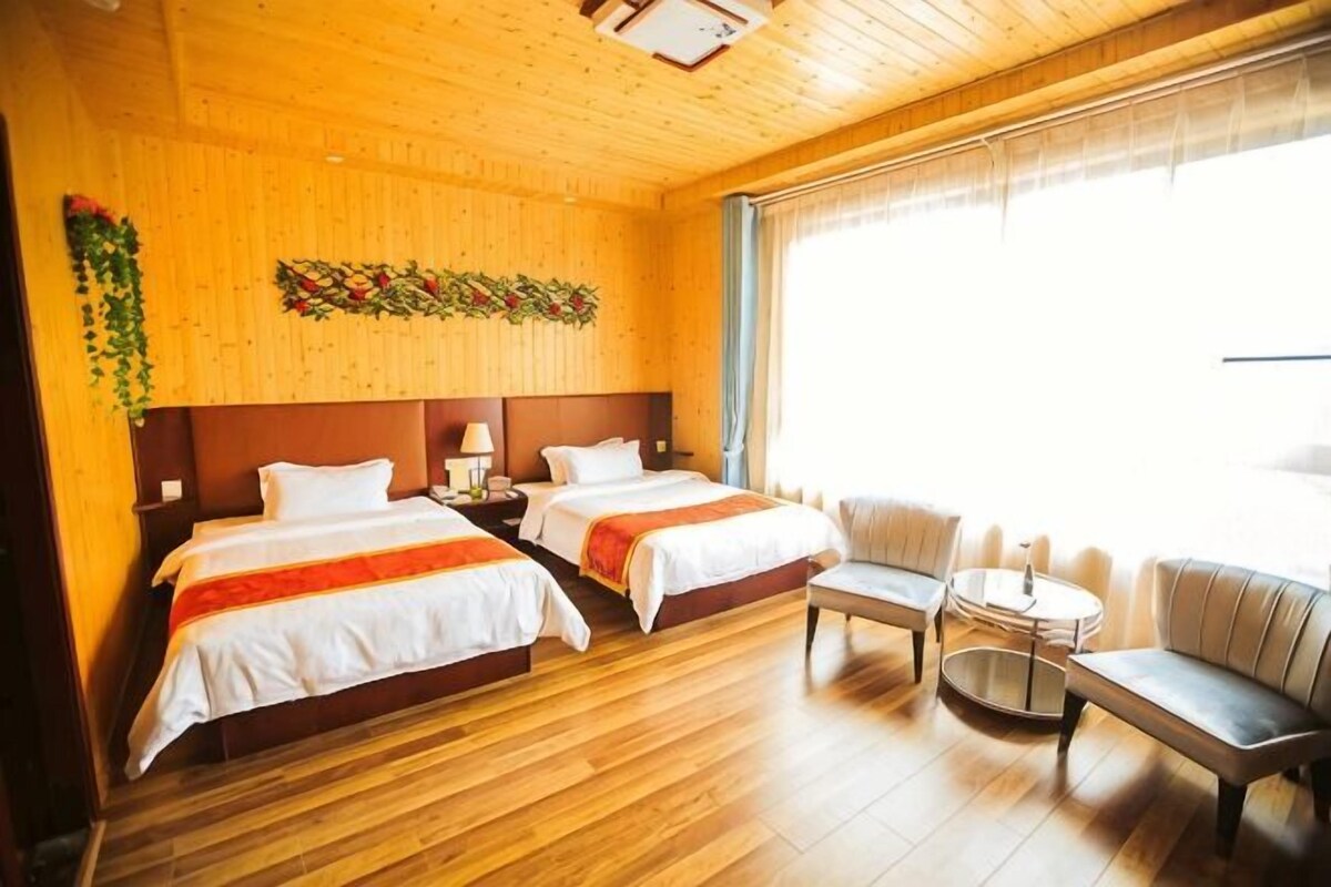 A hotel room with two beds, a sofa, a small round table, and a large window.